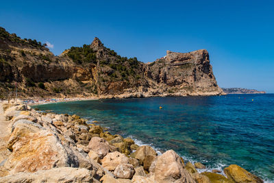 Scenic view of rocks by sea against blue sky