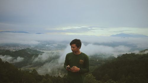 Young man holding mobile phone while standing on mountain