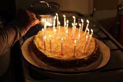 Cropped hand burning birthday candles on cake at home