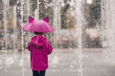 Rear view of girl walking amidst fountain