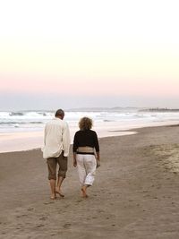 Rear view of couple walking at beach against sky