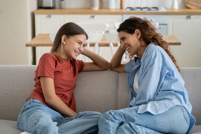 Cheerful friendly woman and teenager daughter are sits on sofa and laughing discussing funny stories