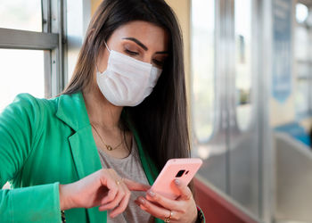 Young woman wearing mask using phone while sitting at subway train