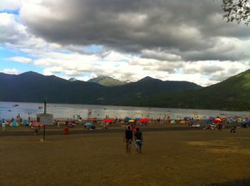 People at beach against cloudy sky