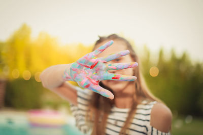 Close-up of girl with messy painted hands against clear sky