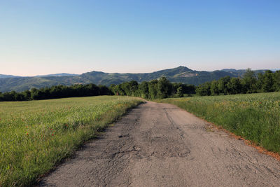 Road amidst field against clear sky