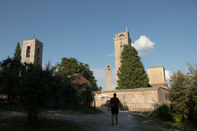 Rear view of woman walking by building against sky