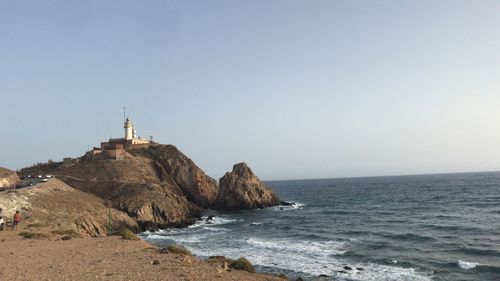 Lighthouse on beach by sea against clear sky