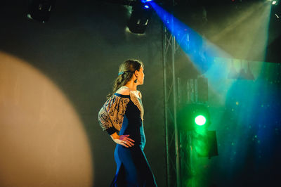 Young woman standing against illuminated wall