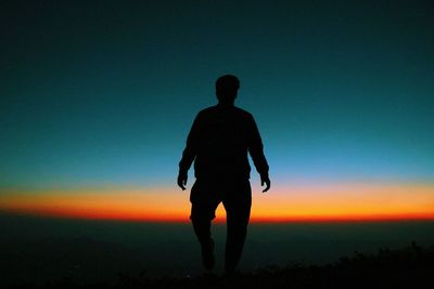 Rear view of silhouette man standing on field against sky during sunset