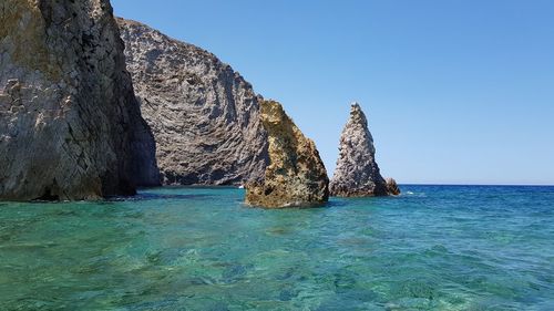 Rock formation in sea against clear blue sky