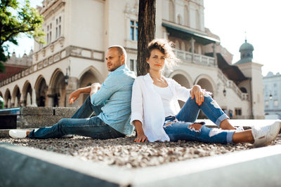 Full length portrait of young man sitting in town square