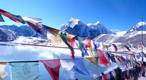 Colorful flags hanging by lake against snow covered mountains