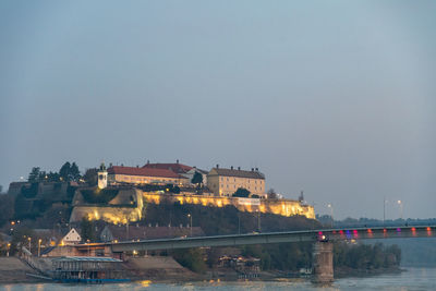 Illuminated buildings by river against sky