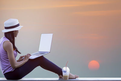 Midsection of woman using mobile phone against sky during sunset