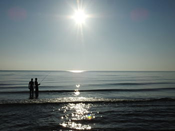 Silhouette people on sea against clear sky