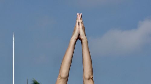 Cropped image of hands clasped against blue sky