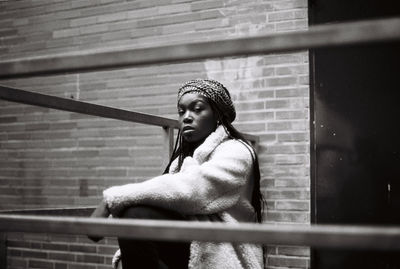 Portrait of young woman sitting against brick wall