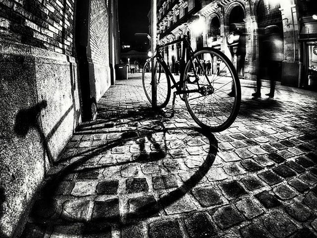 architecture, built structure, building exterior, cobblestone, bicycle, street, the way forward, wall - building feature, paving stone, sidewalk, city, footpath, building, graffiti, brick wall, night, illuminated, shadow, transportation, walkway