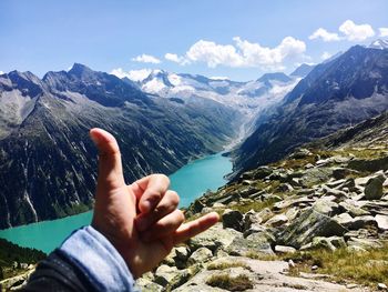 Cropped hand gesturing against river and mountains against sky