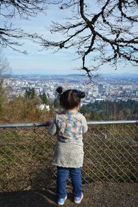 Rear view of girl standing by fence against sky