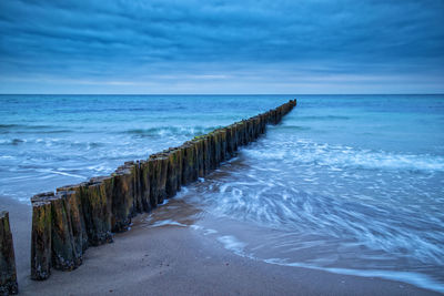 Wooden posts on sea against sky