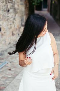 Smiling young woman standing on footpath by wall