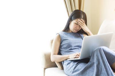 Young woman using mobile phone while sitting on sofa