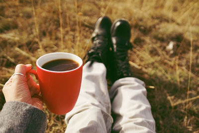 Low section of man holding coffee cup while sitting on grassy field