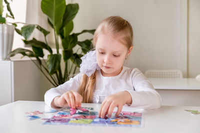 A girl student sits at a desk in the classroom and collects figures / puzzles / small toys 