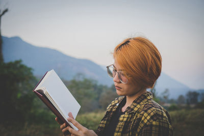 Young woman sitting reading a book at nature in the evening.