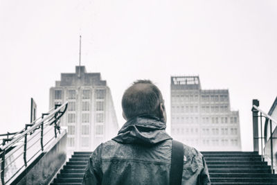 Rear view of man at staircase against sky during rainy season