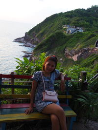 Portrait of young woman sitting on seat against sea