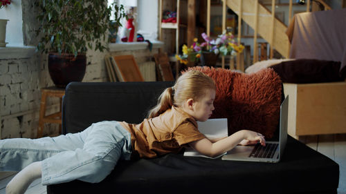 Girl using laptop while lying on sofa at home