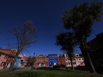 Low angle view of trees and buildings against blue sky