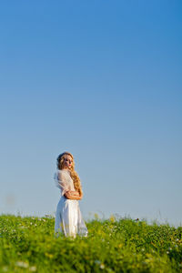 Young woman standing on field against clear blue sky