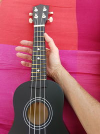 Cropped hand of man holding guitar on bed