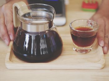 Close-up of person serving black coffee in tray on table