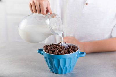 A child pours milk from a jug into a bowl of chocolate flakes. breakfast concept