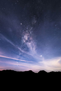 Low angle view of star field over silhouette mountains against sky at night