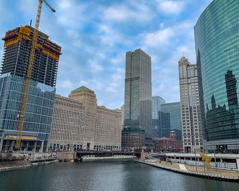 Modern buildings by river against sky in city