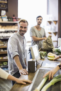Smiling man standing at supermarket checkout counter with friend in background