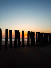 Silhouette wooden posts on beach against clear sky during sunset