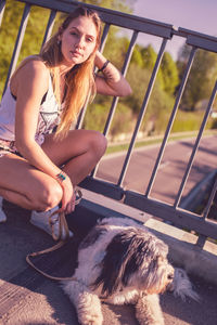 Portrait of young woman crouching by dog on footbridge