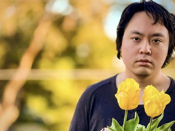 Portrait of young man with yellow tulip flowers against trees at sunset.