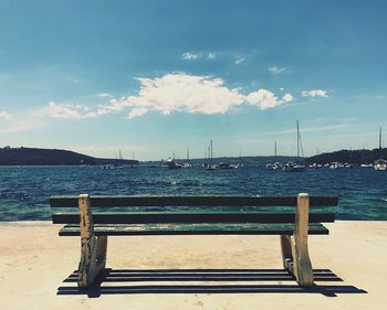 Empty bench on beach against sky