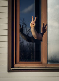 A man shows a victory sign from the window. coronavirus quarantine self-isolation concept