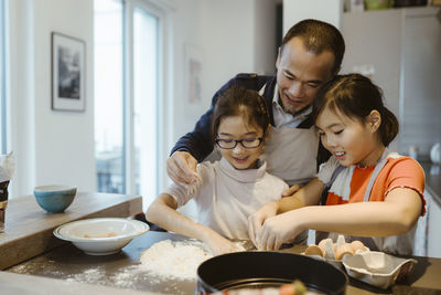 Smiling girls learning to prepare dough with father in kitchen at home