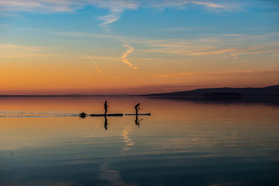 Silhouette people on sea against sky during sunset