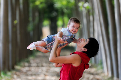 Side view of mother lifting baby boy in mid-air at park